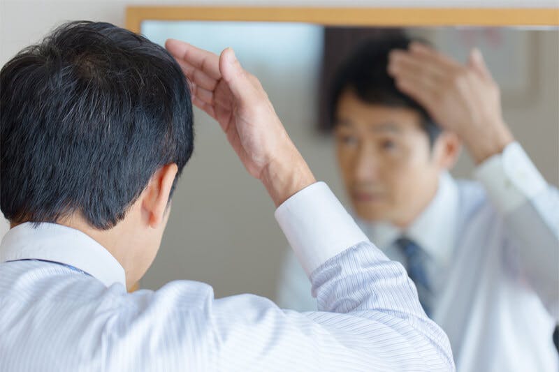 鏡に向かって髪や頭皮の状態をチェックするワイシャツ姿の男性