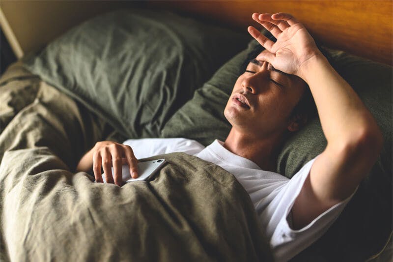 眉間にしわを寄せ寝苦しそうな表情を浮かべる男性