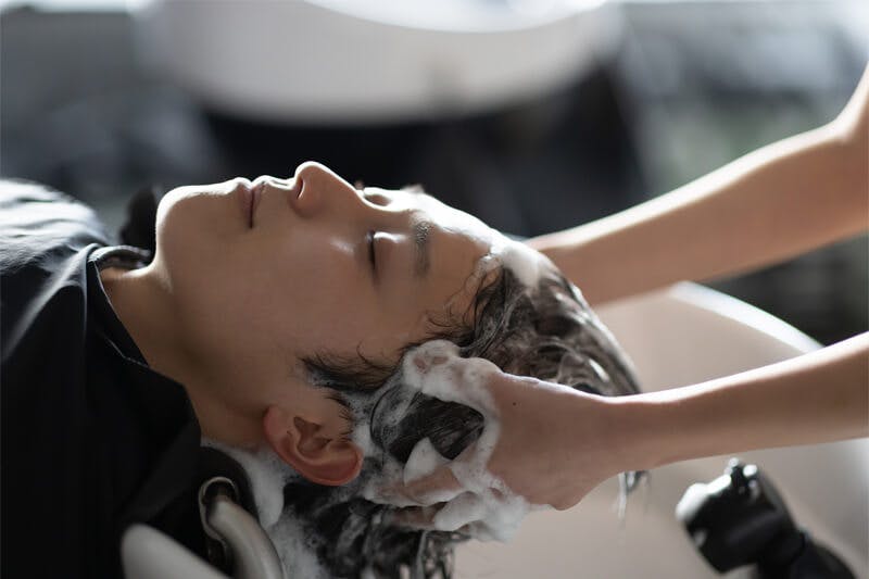 サロンでシャンプーをしてもらい満足そうな笑みを浮かべる男性