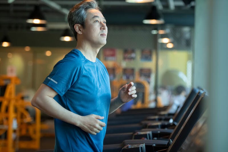 スポーツジムのランニングマシンで運動する男性