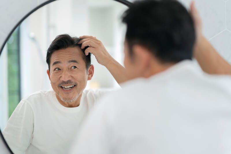 鏡を見ながら髪を触る笑顔の男性