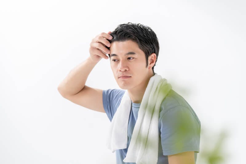 手を生え際にやりながら鏡を見ている男性