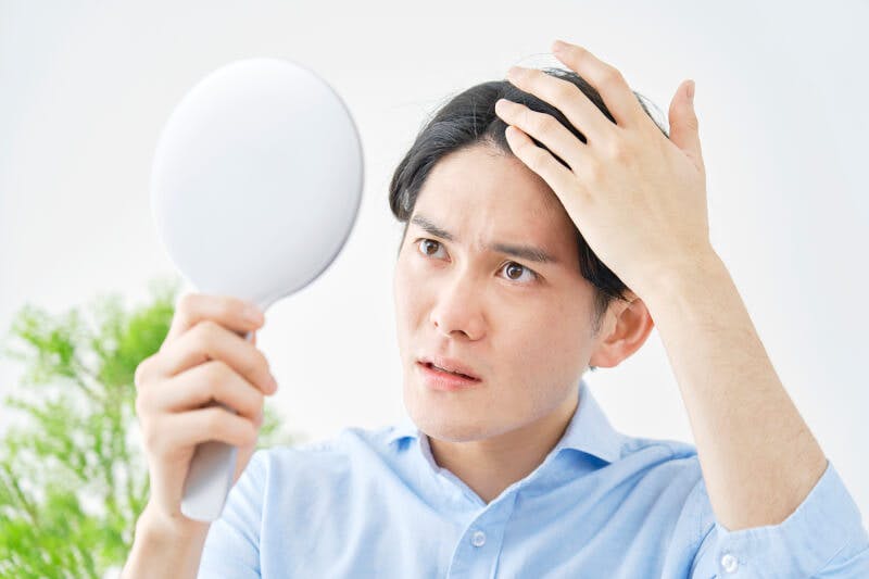 ハンドミラーを持って髪の毛を見る男性