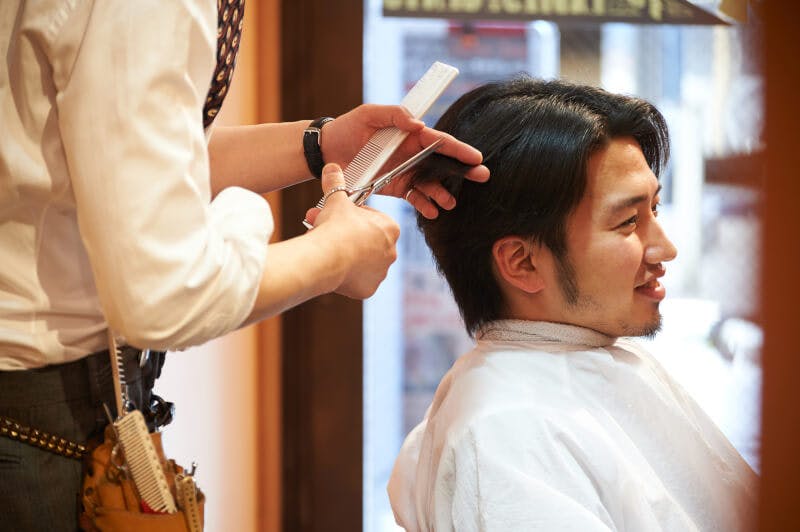 ヘアスタイリストによる施術を受けながら満足そうな笑みを浮かべる男性4