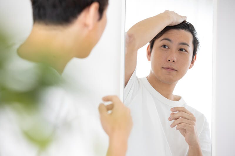 鏡越しに頭皮を気にする男性