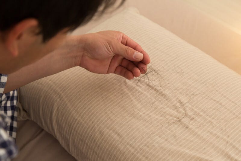 枕につく抜け毛を手に取る男性の後ろ姿