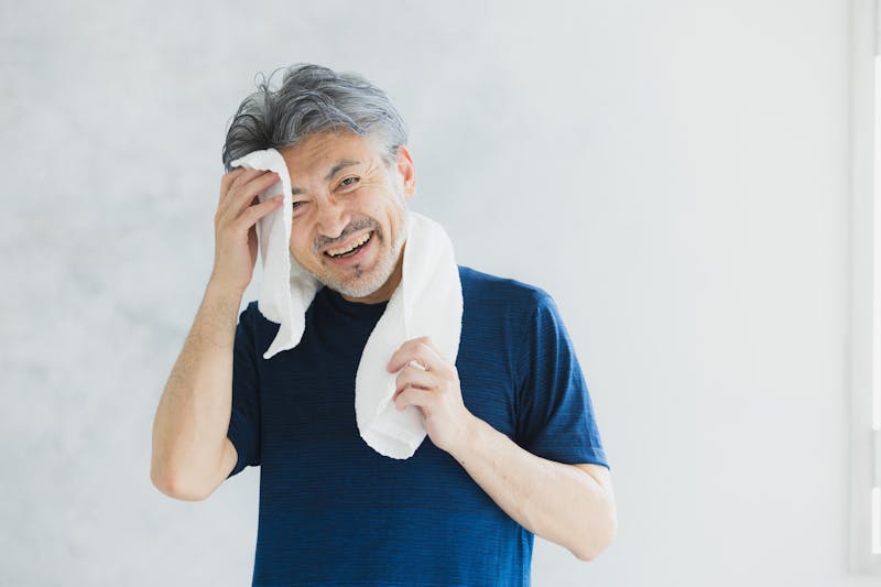タオルで汗を拭き笑顔を浮かべる運動後の男性
