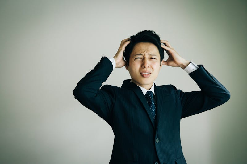 今にも泣き出しそうな表情で頭を抱えるビジネスパーソン
