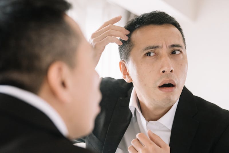 薄毛や白髪の状態を鏡に寄ってチェックするビジネスパーソン