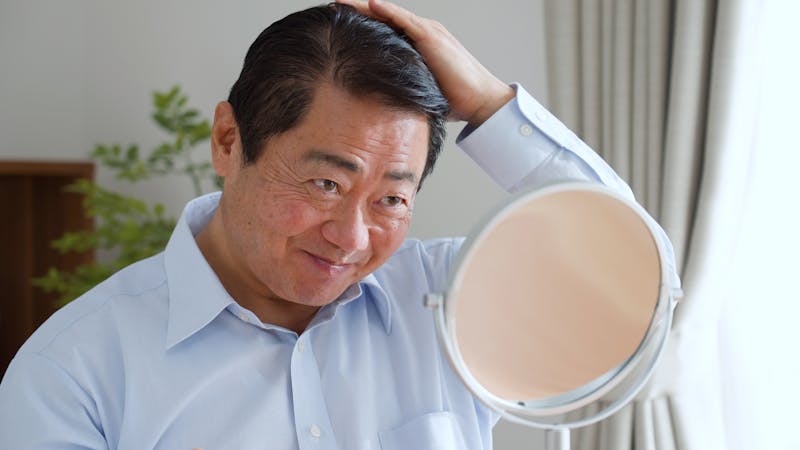 鏡越しに髪を触り笑みを浮かべる男性