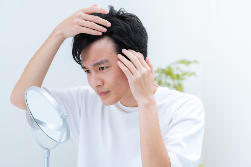 鏡を見て生え際を気にする男性