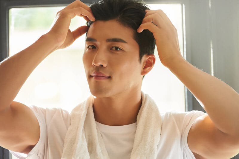 首にタオルをかけて髪を触る男性
