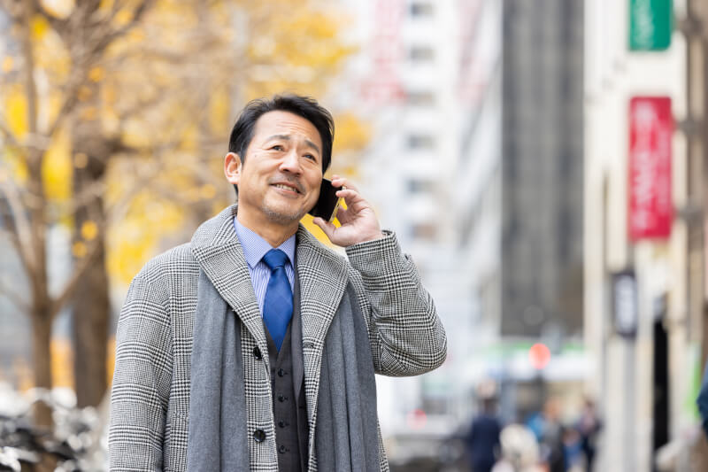 コートとマフラーを身に着けてスマートフォンで通話する男性ビジネスパーソン