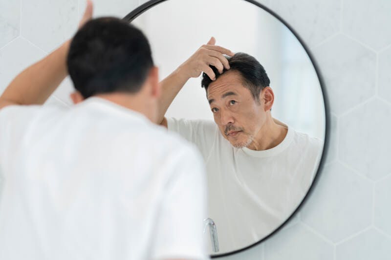 髪の毛を触りながら鏡を見る男性