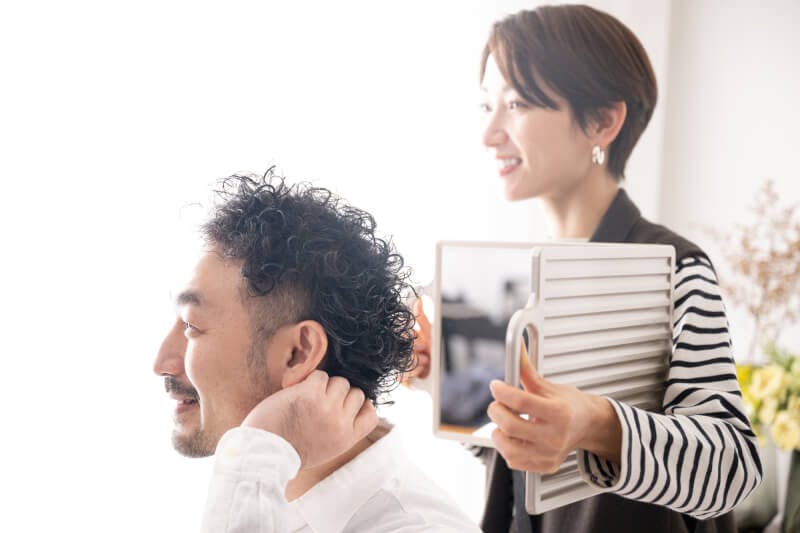 美容院で髪の毛の仕上がりを鏡で見せる女性と、それを見る男性
