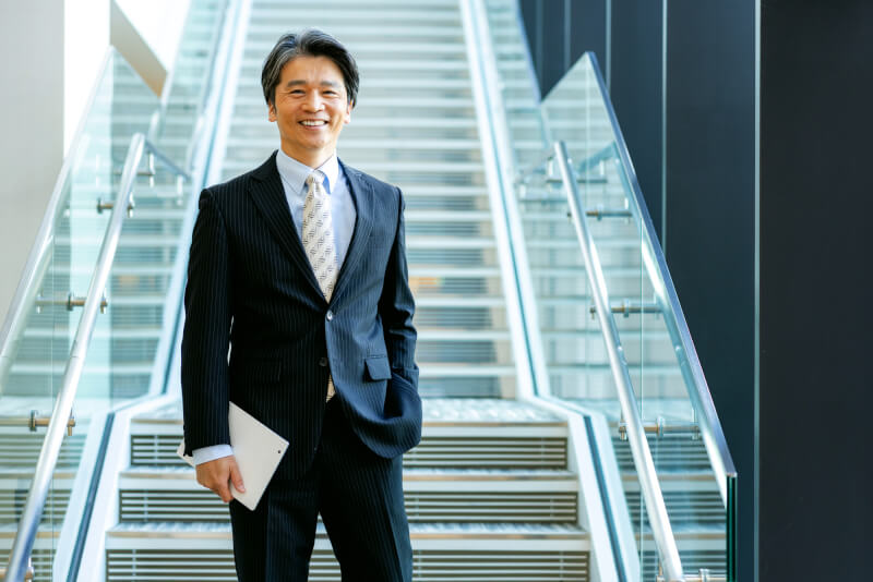 階段の前で笑顔を見せる男性ビジネスパーソン
